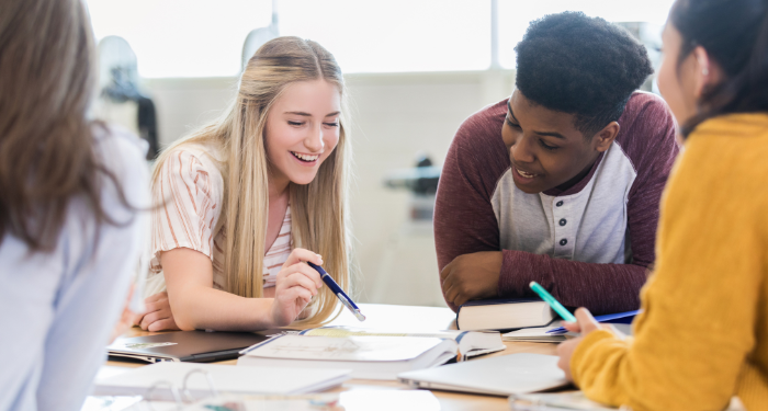 a photo of a group of teens talking over an open book