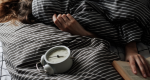 a photo of a person under blankets with an alarm clock and book beside them
