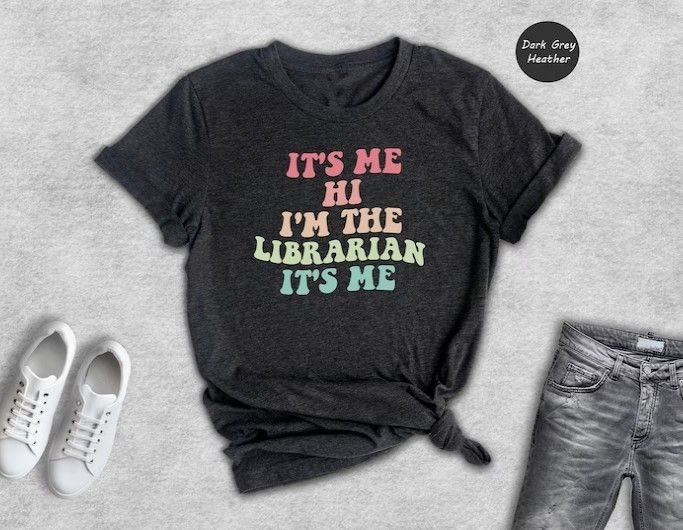 T-shirt with retro rainbow colored text reading "It's me Hi I'm the librarian it's me"