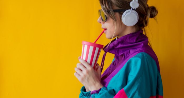 white woman dressed in '90s clothing drinking from a red and white cup