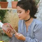 a lighter-skinned Asian woman reading by some potted plants