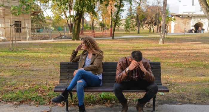 a white man and woman sitting on a park bench seemingly at odds with each other and facing away from each other