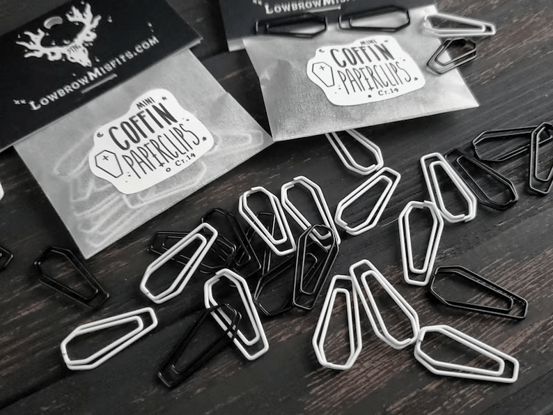 Photo of a bunch of black and white paper clips shaped like a coffin strewn across a table. 