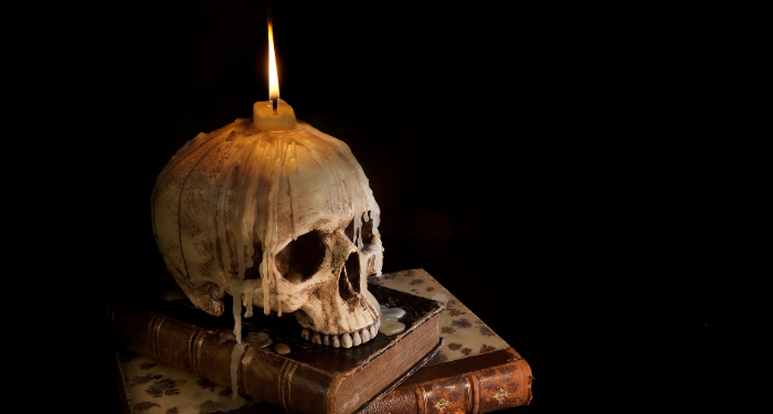 a photo of a skull resting on a stack of books. It has a candle on top of it with wax dripping down.