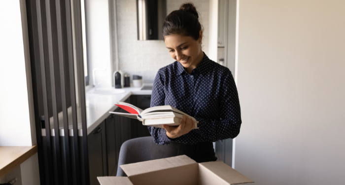 a photo of a woman with brown skin smiling as she pulls a book out of a box