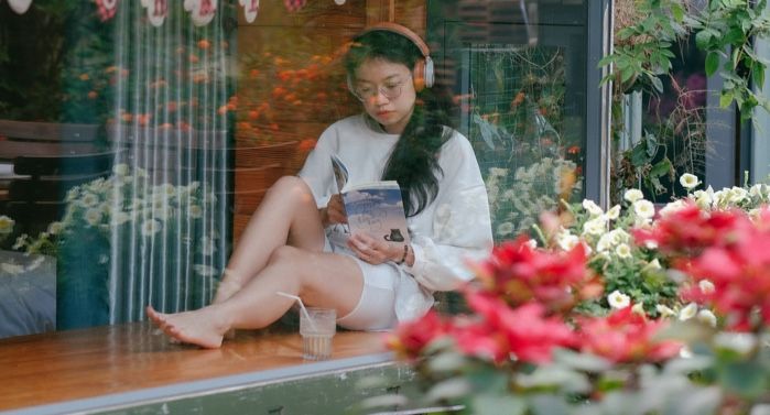 fair-skinned Asian woman reading near storefront window and flowers with her shoes off, relaxing