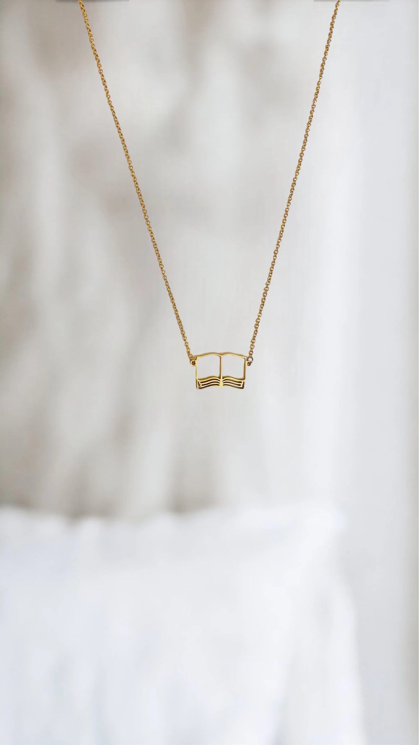 A golden open book necklace in front of a white background.