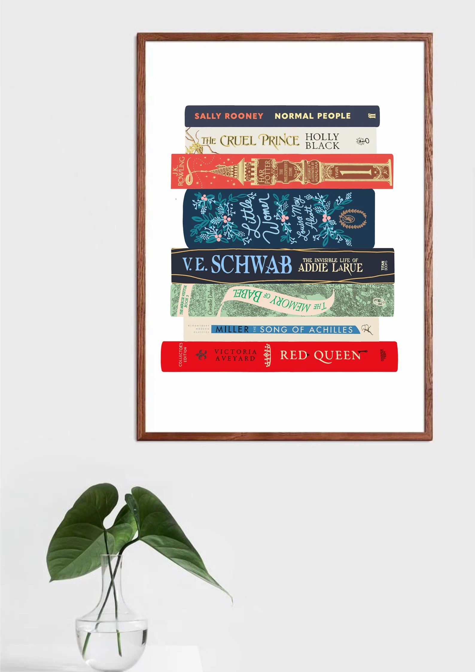 Custom book stack art print in a frame on a white wall in front of a plant.