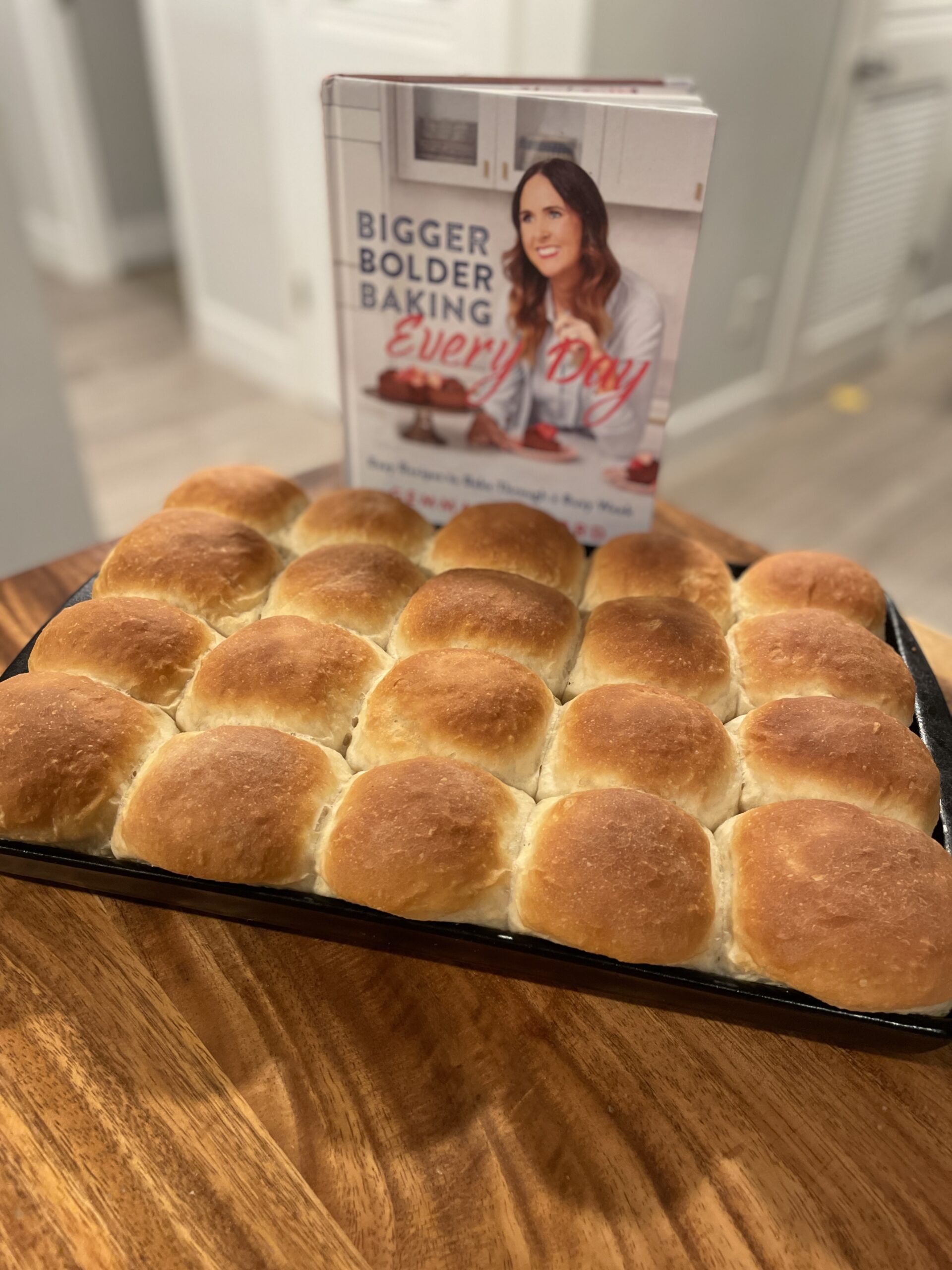 A tray of puffy, golden brown rolls in front of the cookbook Bigger Bolder Baking Every Day
