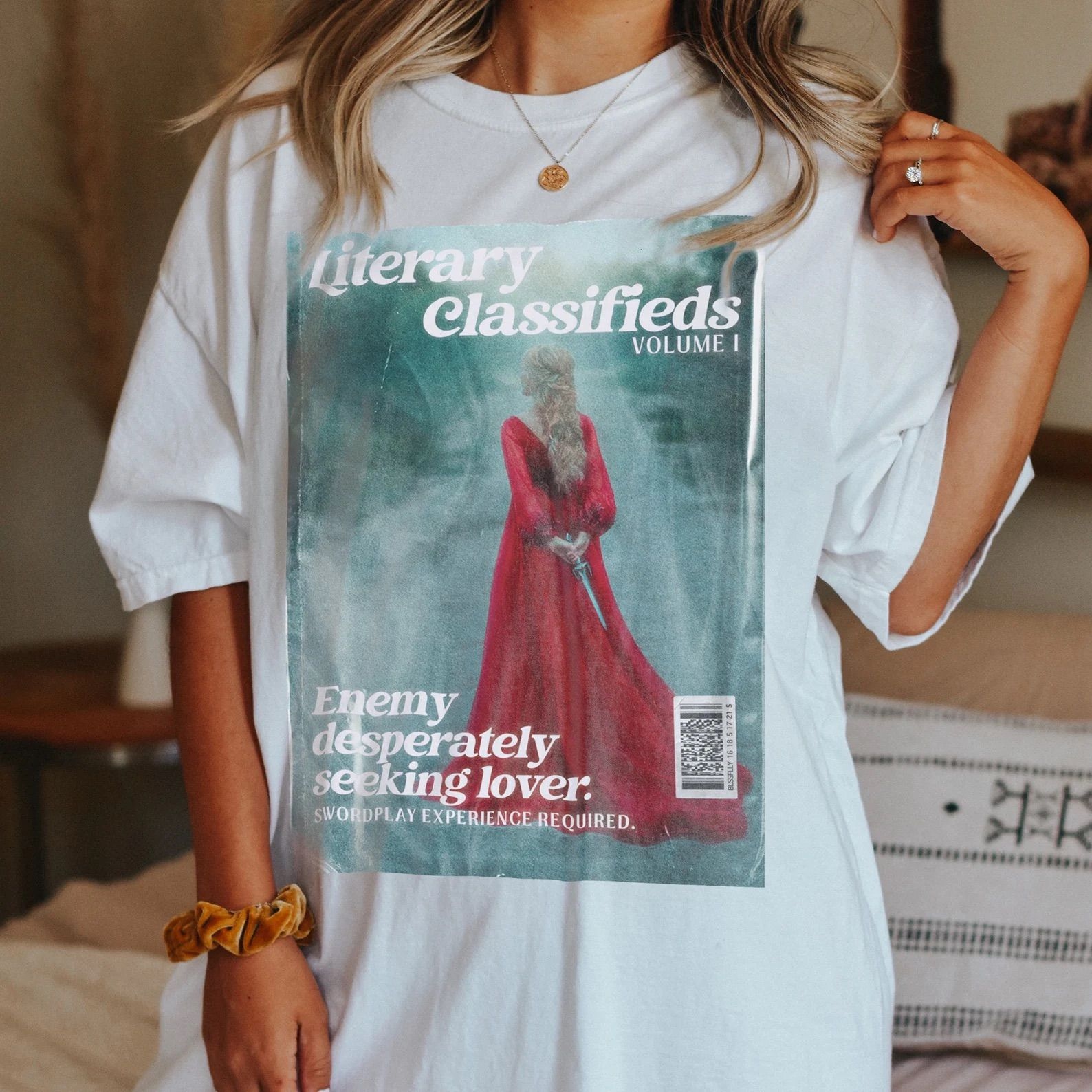 Literary Classifieds- Enemies to Lovers t-shirt on a white model with blond hair in a bedroom.
