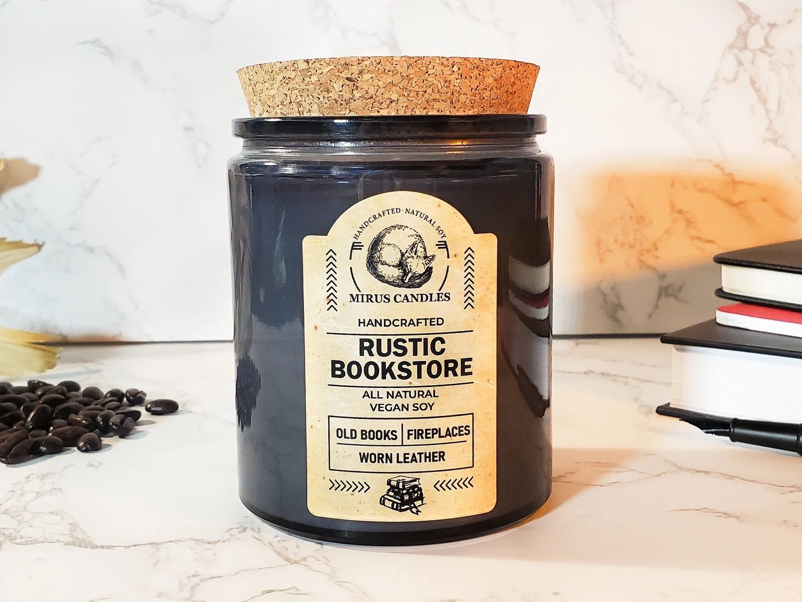 A Rustic Bookstore Soy Candle is on a table with a stack of books.