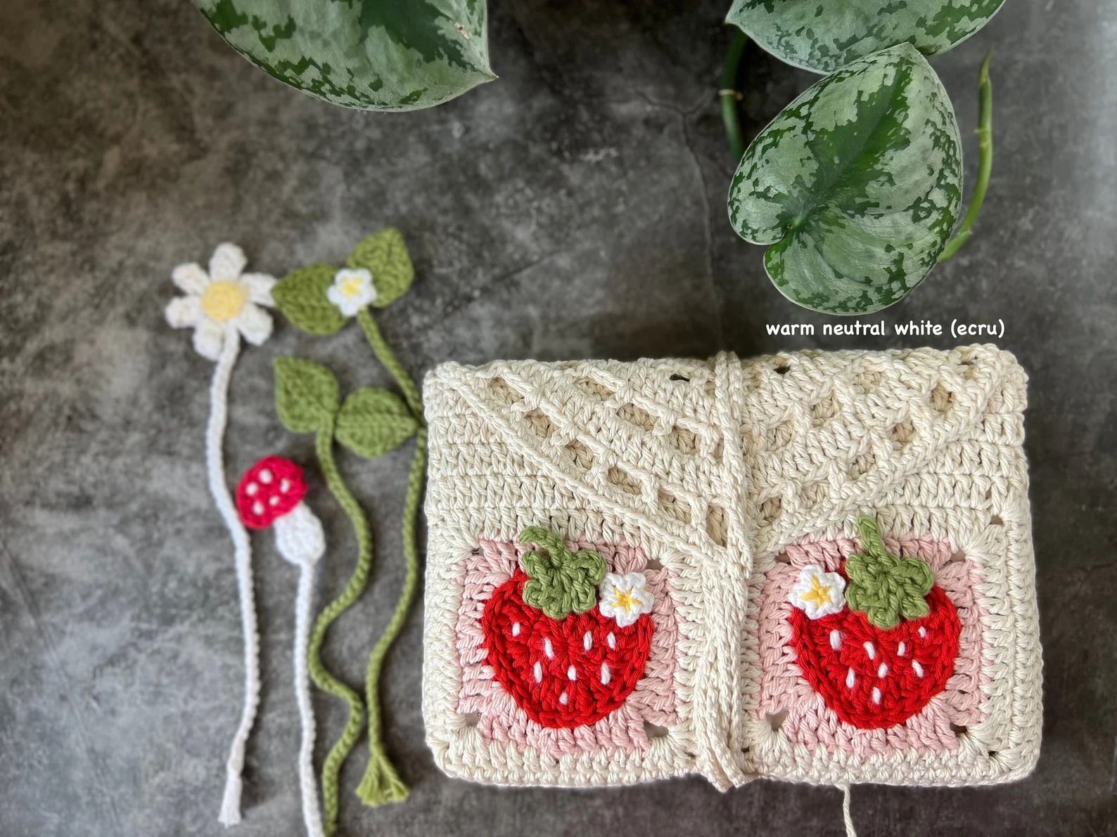 Crochet Handmade Book Sleeve with Red Strawberries is on a gray background with crochet bookmarks.
