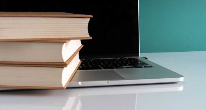 a stack of three books resting on the keyboard of an open laptop