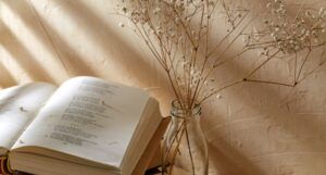an open book of petry next to a vase of dry flowers