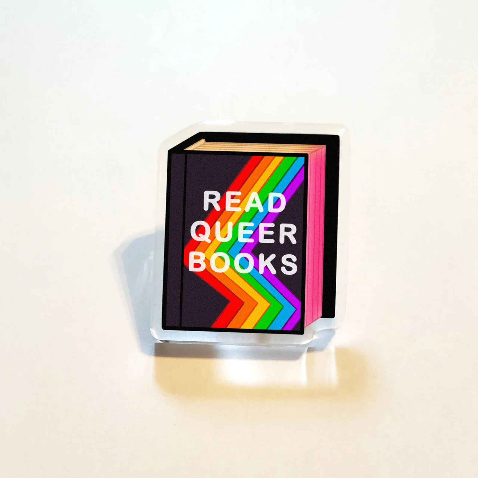 Image of an acrylic pin in black that says "read queer books."
