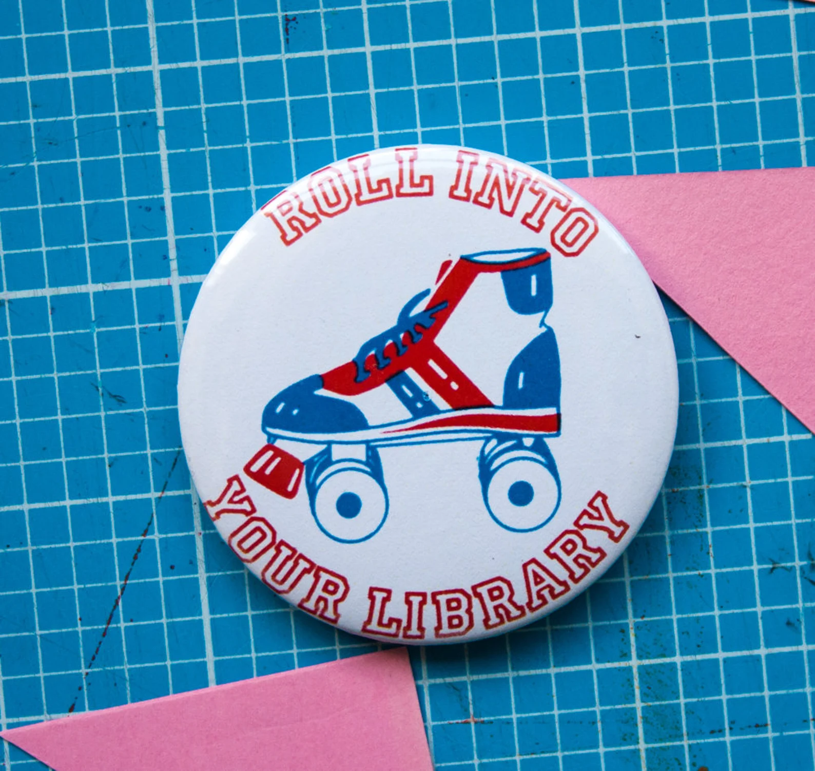 Image of  pin that says "roll into your library" and has a roller skate. 