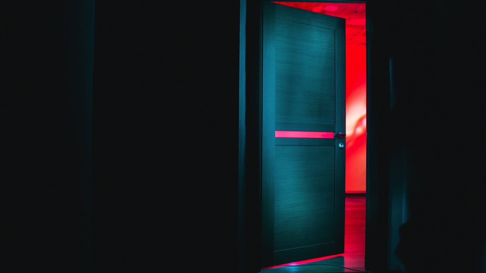 red neon light behind a partially open door in a dark hallway