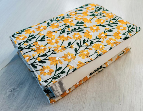 An embroidered notebook cover featuring leaves and yellow daisies.