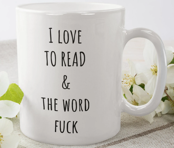 a white cofee mug with black lettering that says "I love to read & the word fuck"