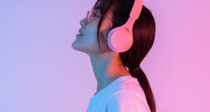 fair-skinned Asian person with long hair wearing headphones against a pink and lilac background
