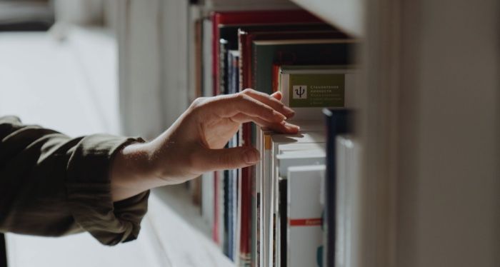 fair-skinned hand reaching for a book on a shelf