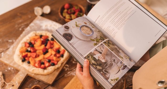 fair-skinned hands holding open a cookbook in front of an assembled pastry