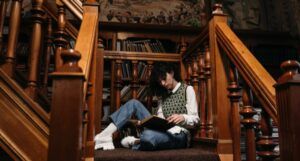 fair-skinned person sitting on wooden staircase reading a book