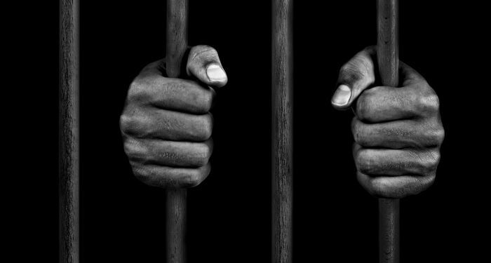 brown-skinned hands of a prisoner gripping the bars of a jail cell