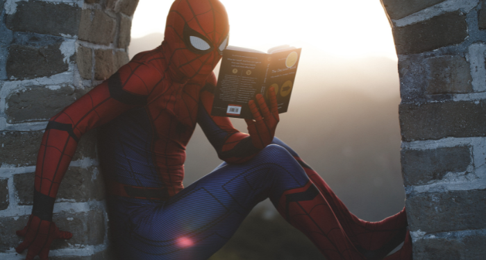 a photo of someone dressed as Spider-Man reading outside