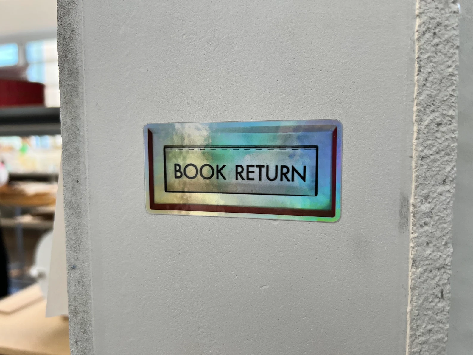 Image of a sticker that looks like a book return slot. 