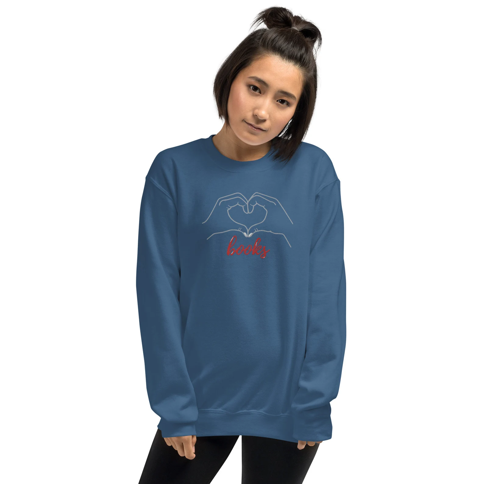 Image of a woman with olive skin wearing a blue sweatshirt. The sweatshirt has white embroidery of a heart made from two hands with the word "books" below. 