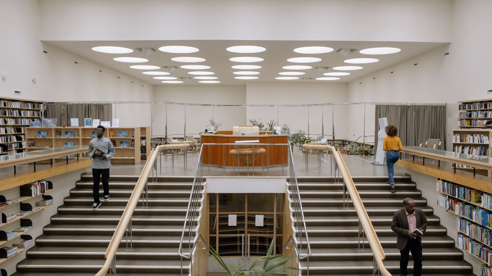 Image of the inside of a library with two big staircases. Three Black people are using the stairs. 