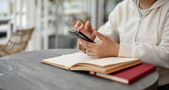 a person scrolling on their phone over a stack of two notebooks