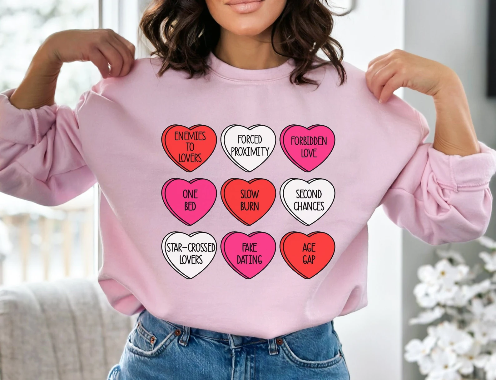 Image of a pink sweatshirt with hearts on it. Inside the hearts are romance trope names. 