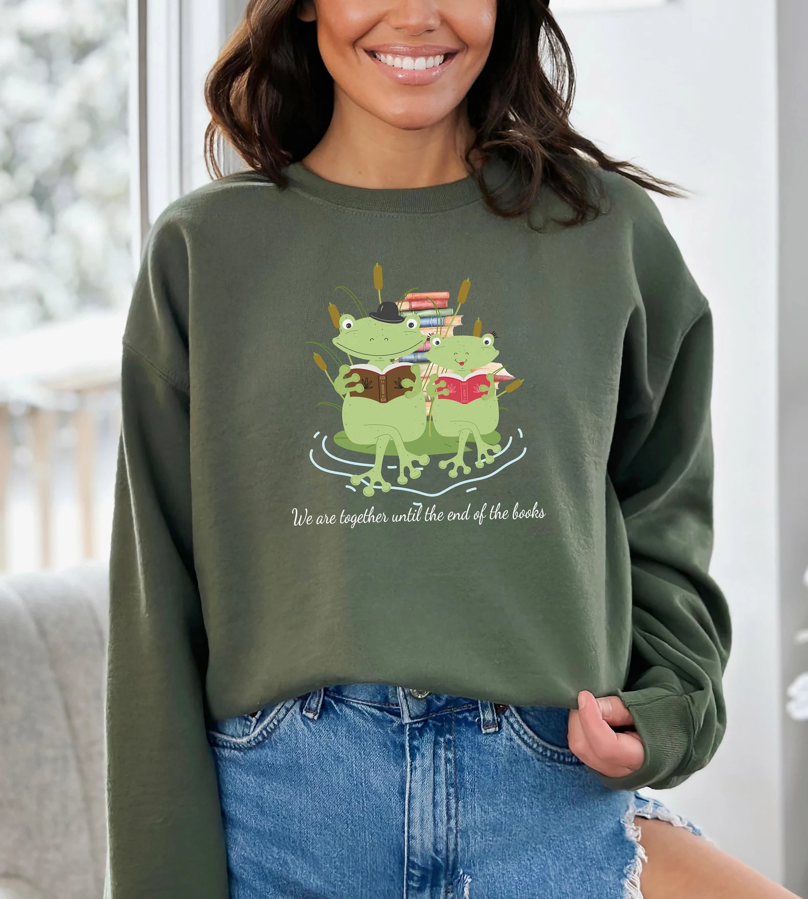Image of a green sweatshirt with an image of two frogs reading a pile of books. It says "we are together until the end of the books" beneath the frogs. 