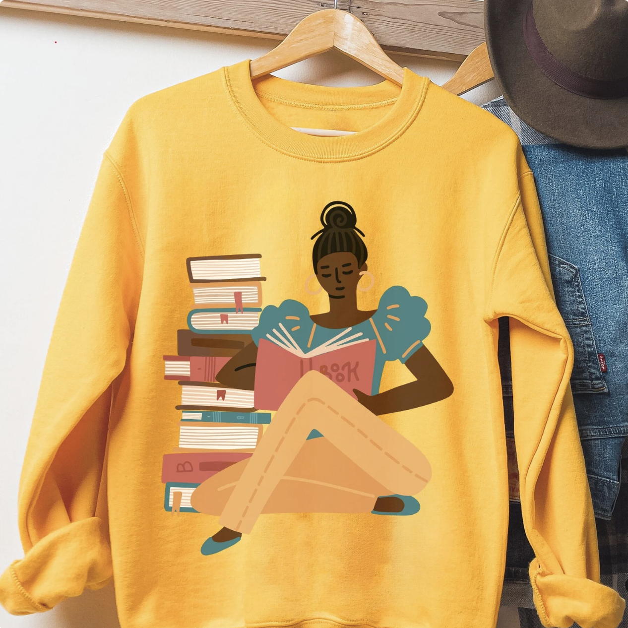Yellow sweatshirt with a design of a brown-skinned Black woman reading