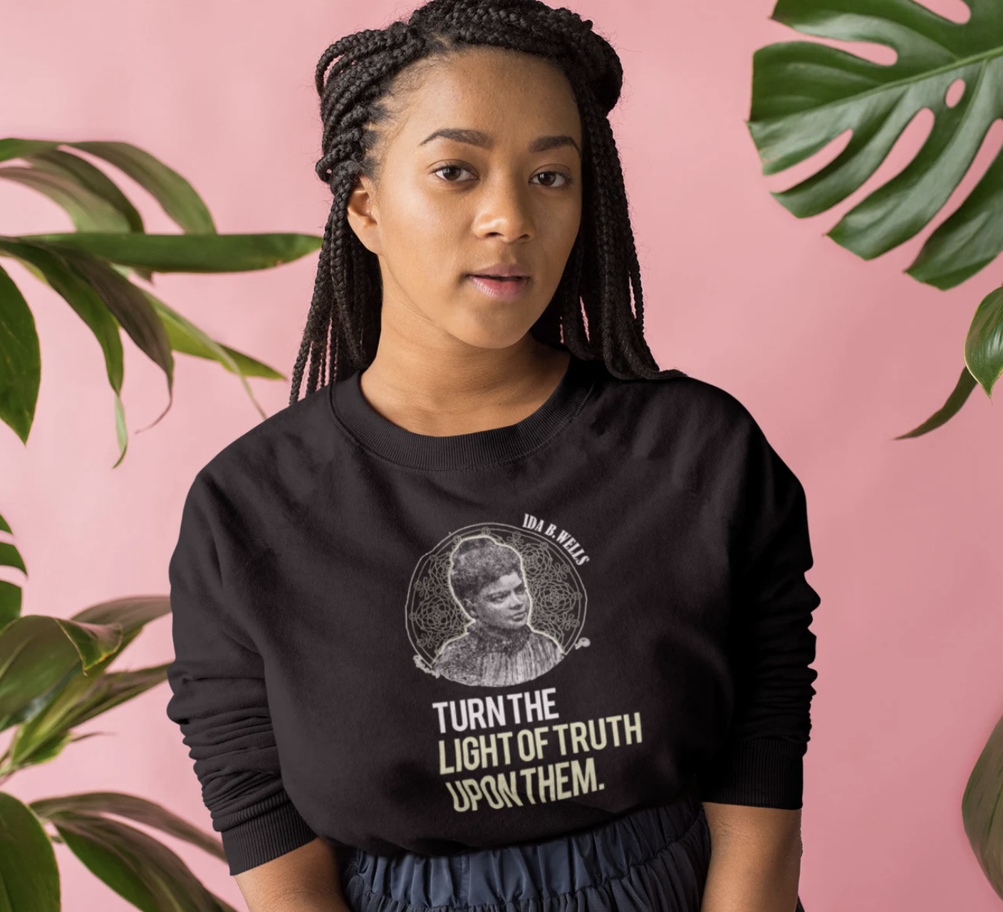 A light brown-skinned Black woman wearing a black sweatshirt with an Ida B Wells quote on it