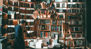 a photo of a man browsing a table at a bookstore with a light feature made of books overhead