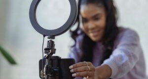 brown-skinned Black woman with long, curly hair adjusting a phone to record content