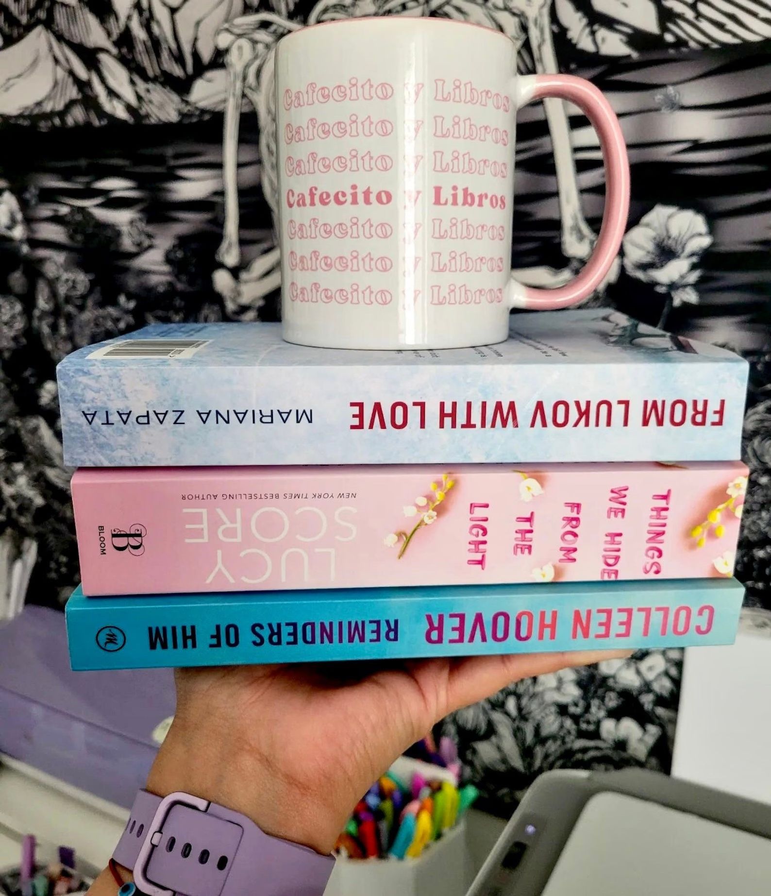 a pink and white mug on top of a stack of three books. The pink text on the mug reads "cafecito y libros"