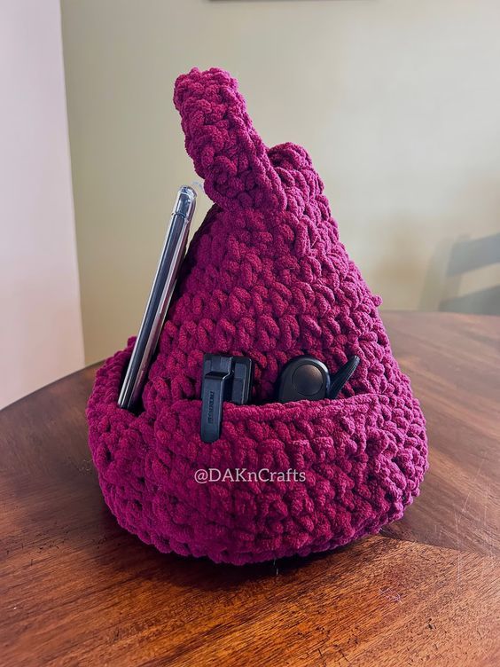 a pear-shaped pillow crocheted in chunky fuschia yarn with a pocket for a kindle and a side pocket for accessories 