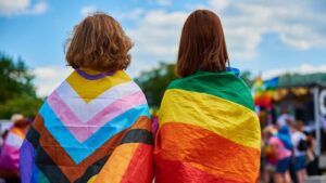 Image of two young people with rainbow pride flags draped over their shoulders