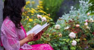 light-skinned woman of color reading in a pink dress in a garden