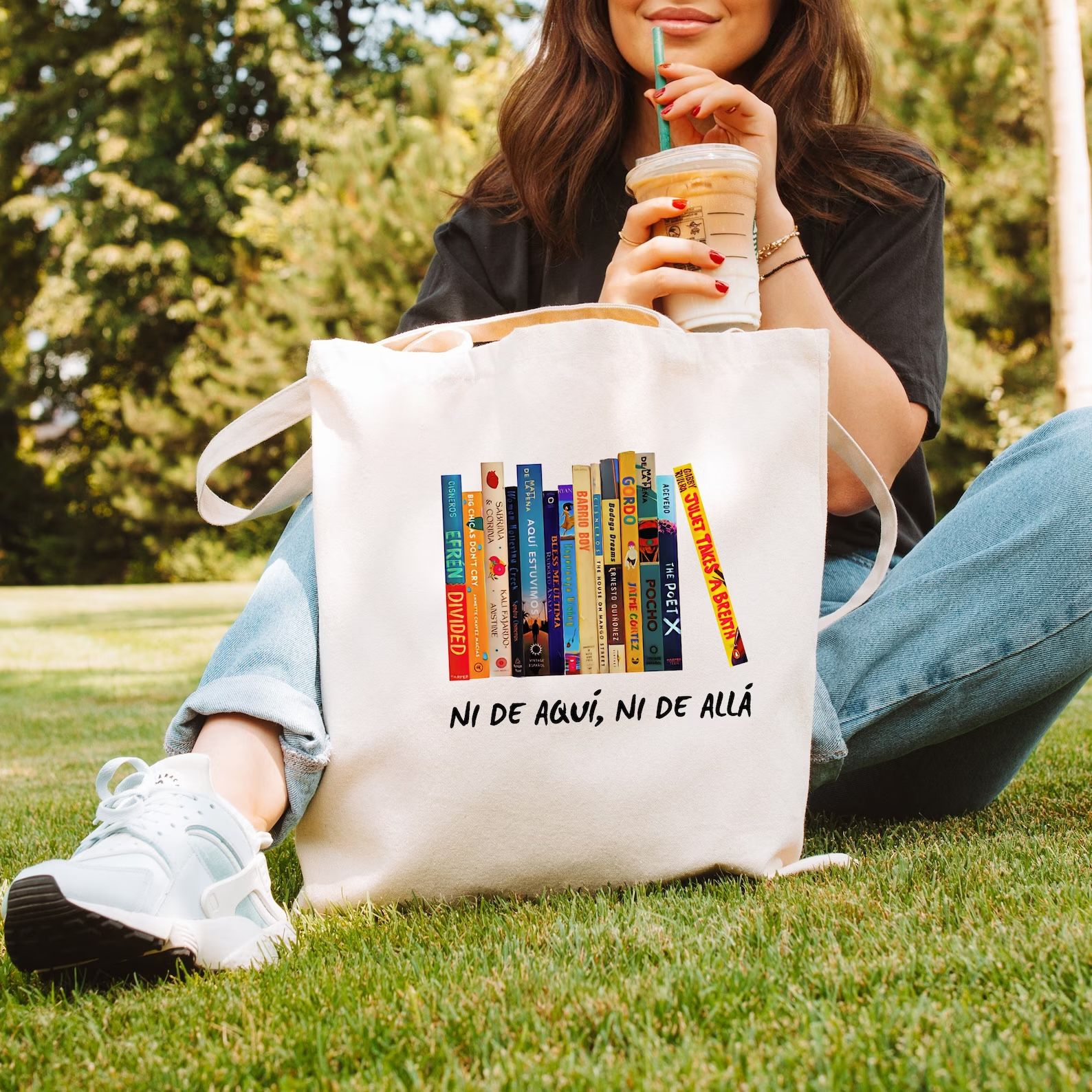canvas tote bag with a design of colorful book spines. Beneath the books are the words "ni de aqui, ni de alla"