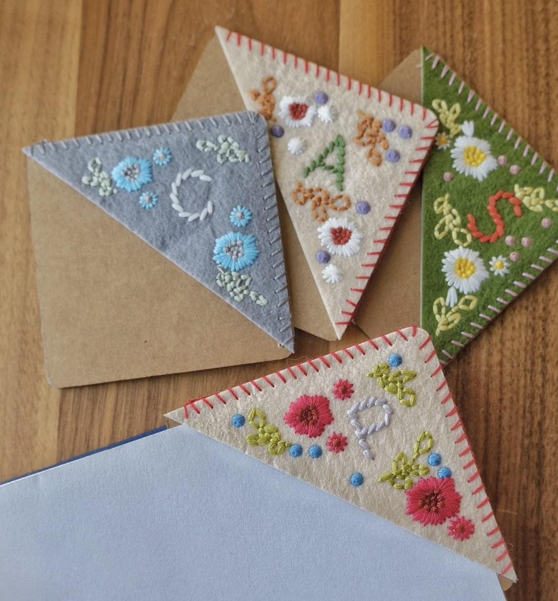 Four felt corner bookmarks embroidered with floral designs and initials