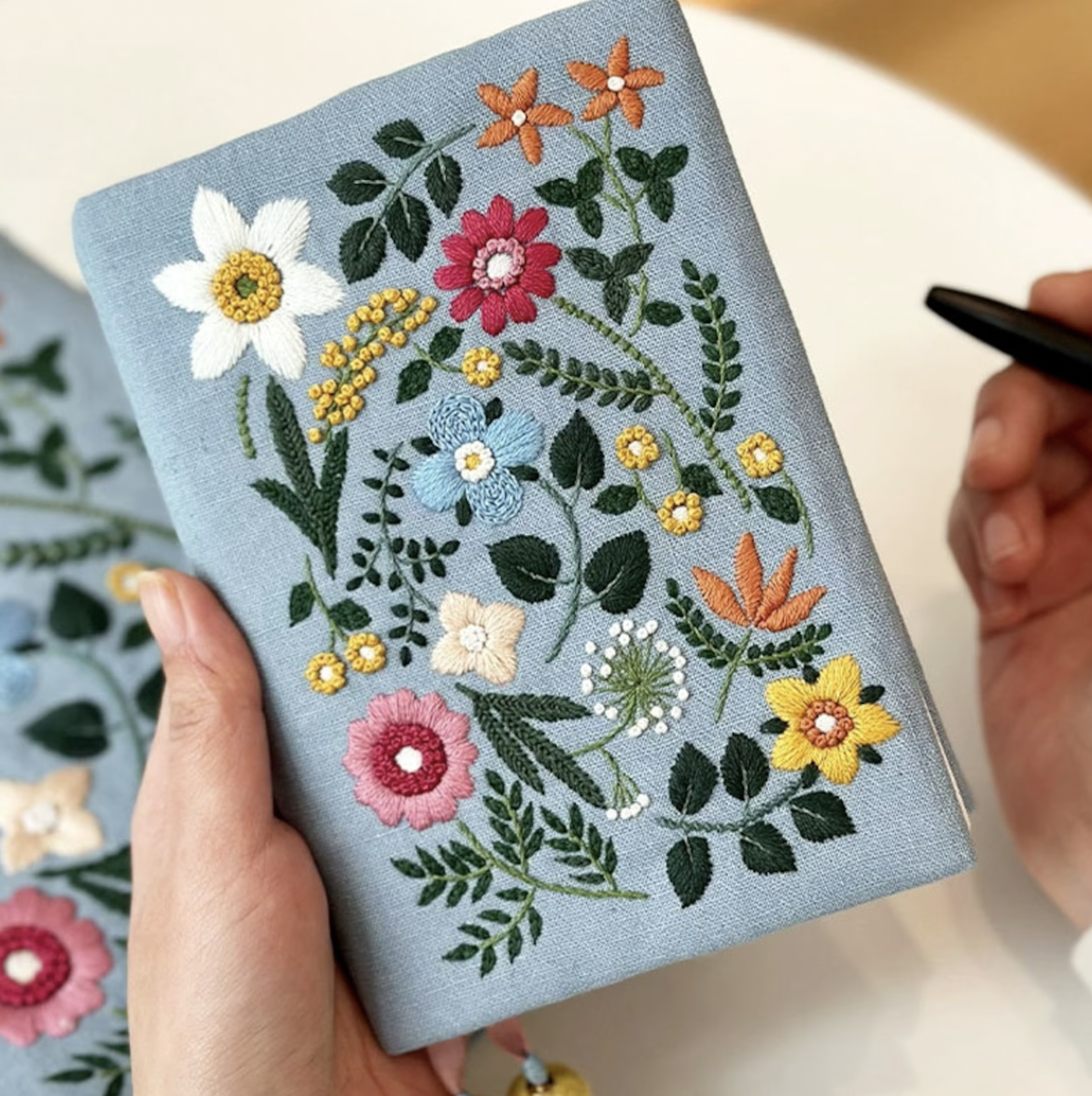 Image of a light blue fabric book cover with floral embroidery