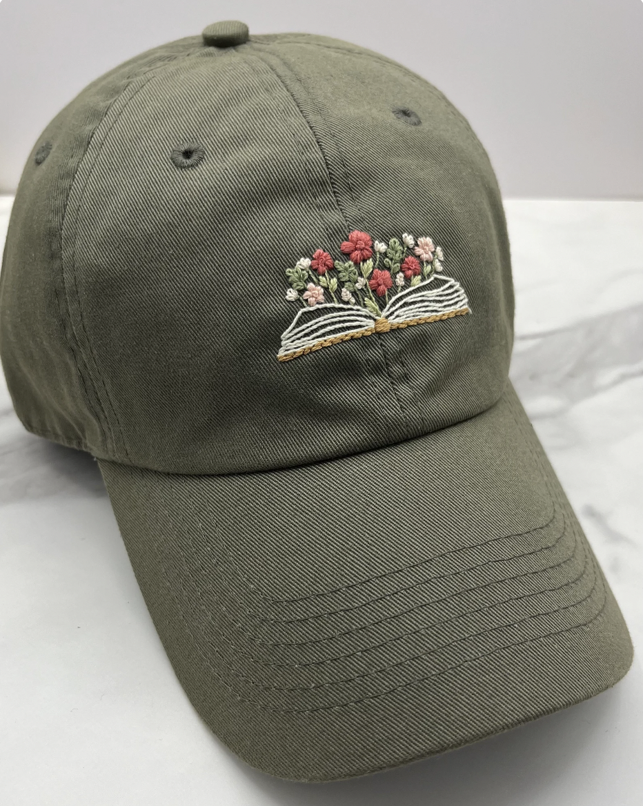 Image of an olive green baseball hat with an embroidered open book and flowers