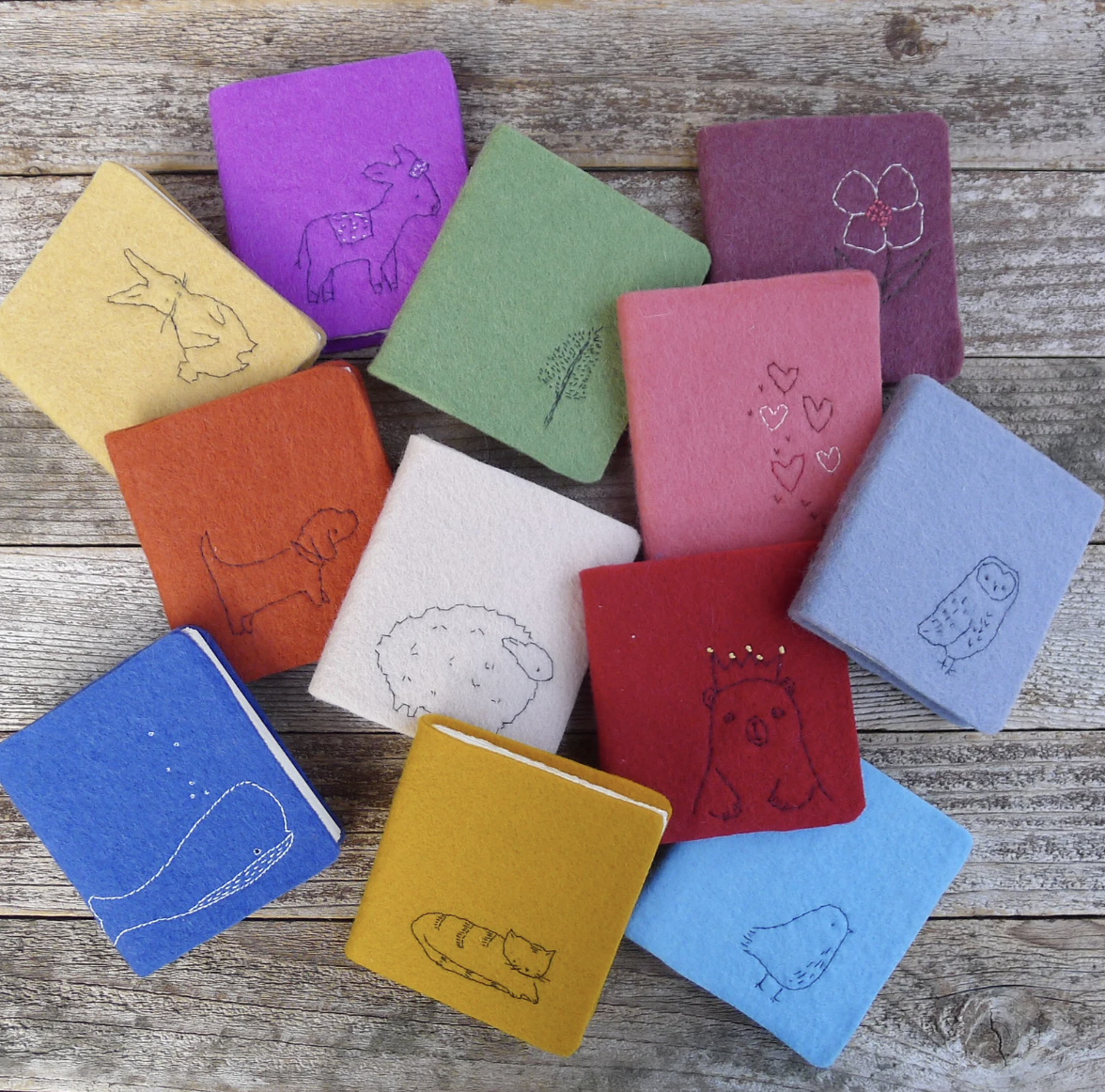 Image of a bunch of colorful mini-journals covered in wool with minimalist embroidered animal designs
