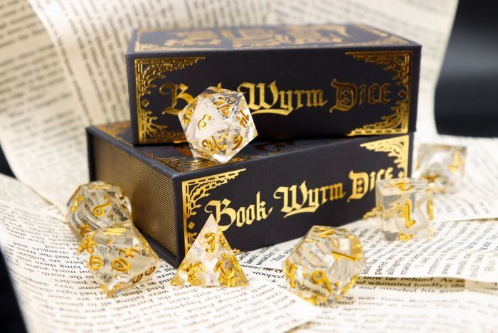 a set of clear dice, including a D20, with scraps of papers inside and gold numbers, in front of a box with the text Book Wyrm Dice