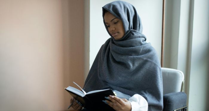 brown-skinned Black woman wearing a hijab and reading
